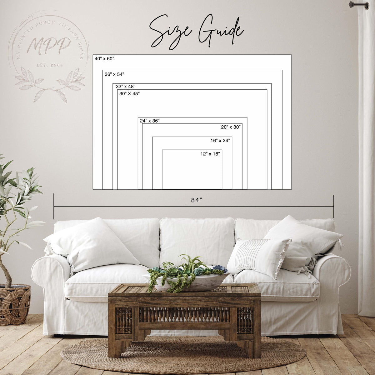 a living room with a white sofa, a wooden coffee table, and a potted plant. Above the sofa, there is a size guide with dimensions and a logo for a company.